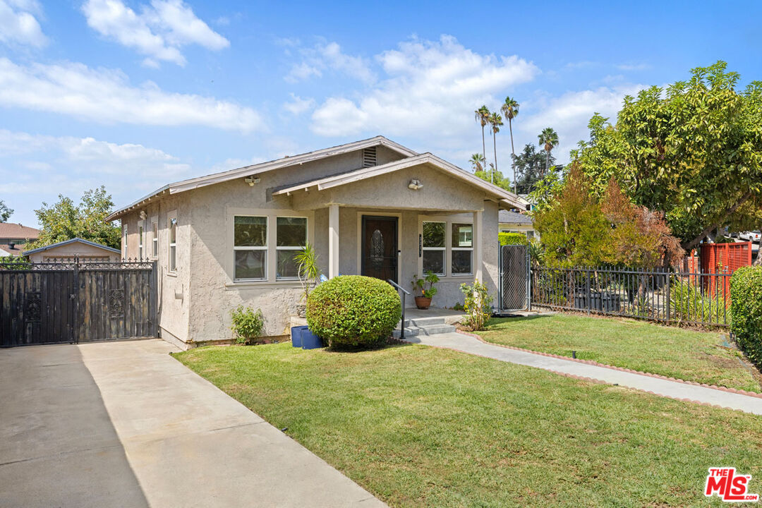Single-story stucco home with a front lawn, driveway, and gated side entrance.