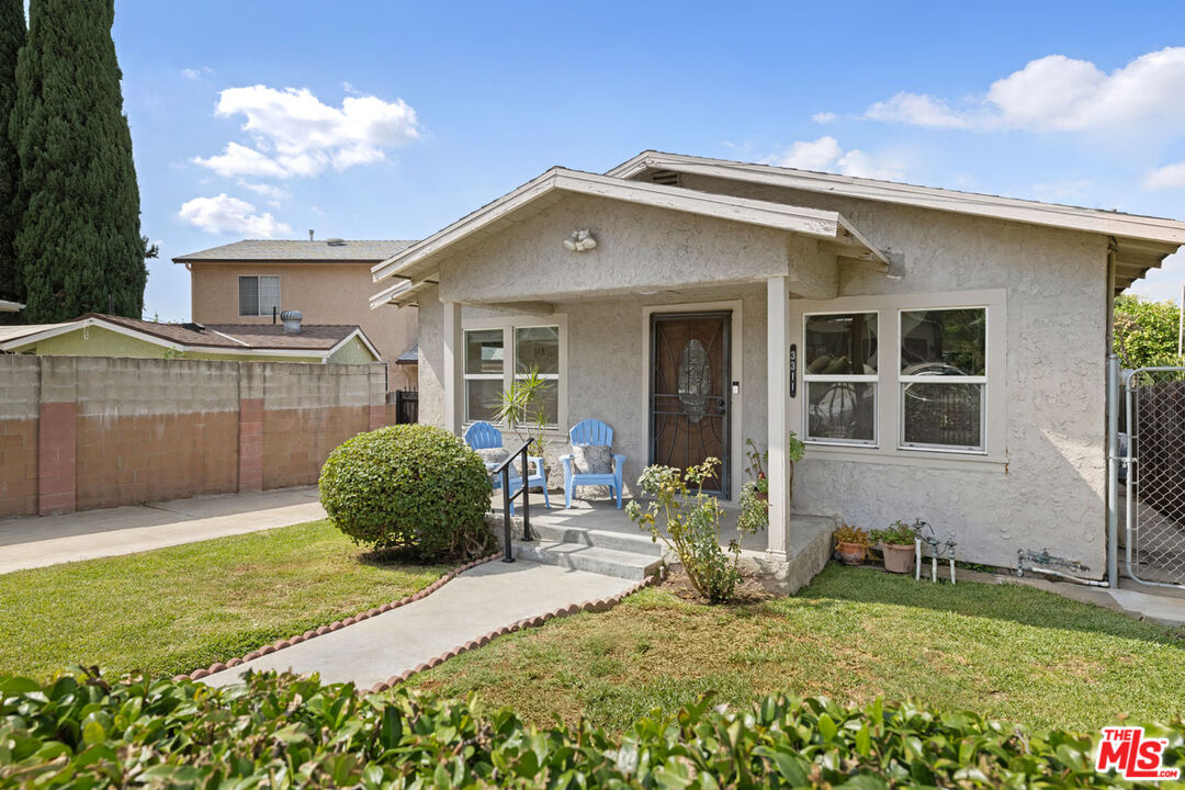 Single-story stucco house with blue porch chairs and a curved walkway across the front lawn.