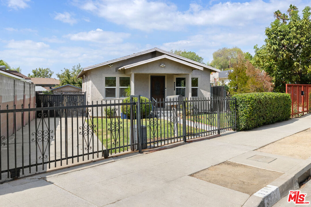 Single-story gray home with a gabled roof behind a black iron gate and small front lawn.