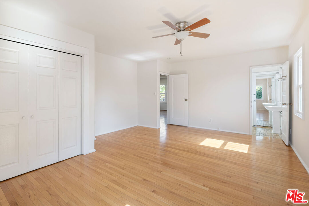 Empty bedroom with hardwood floors, ceiling fan, closet, and adjoining bathroom.