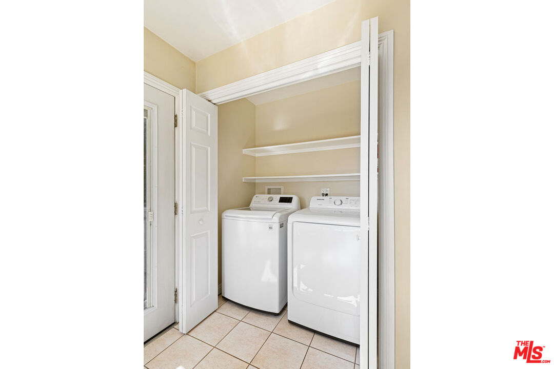 Laundry closet with a white washer and dryer beneath two shelves.