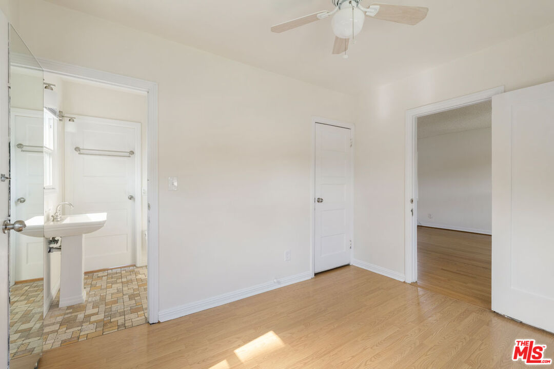Empty bedroom with hardwood floors, a ceiling fan, and an adjoining bathroom.
