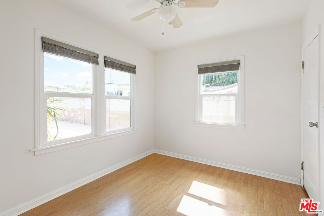 Empty bedroom with light wood flooring, three windows, and a ceiling fan.