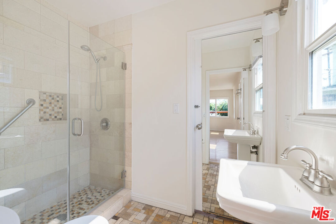 Bathroom with a glass shower, mosaic tile floor, and white pedestal sink beside a window.