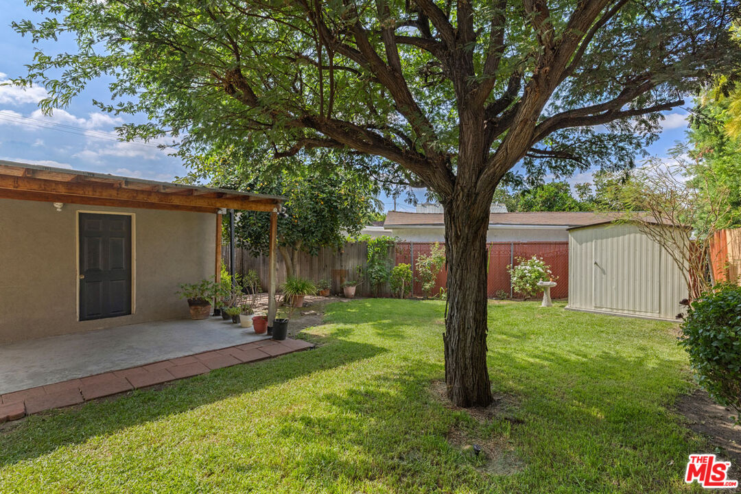 Backyard with a large shade tree, lawn, covered patio, and white shed.