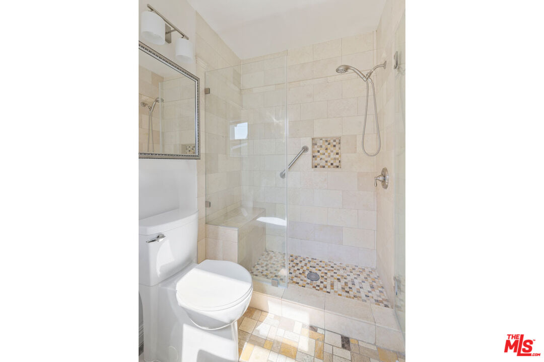 Tiled bathroom with a glass shower, built-in bench, mosaic accents, and toilet.