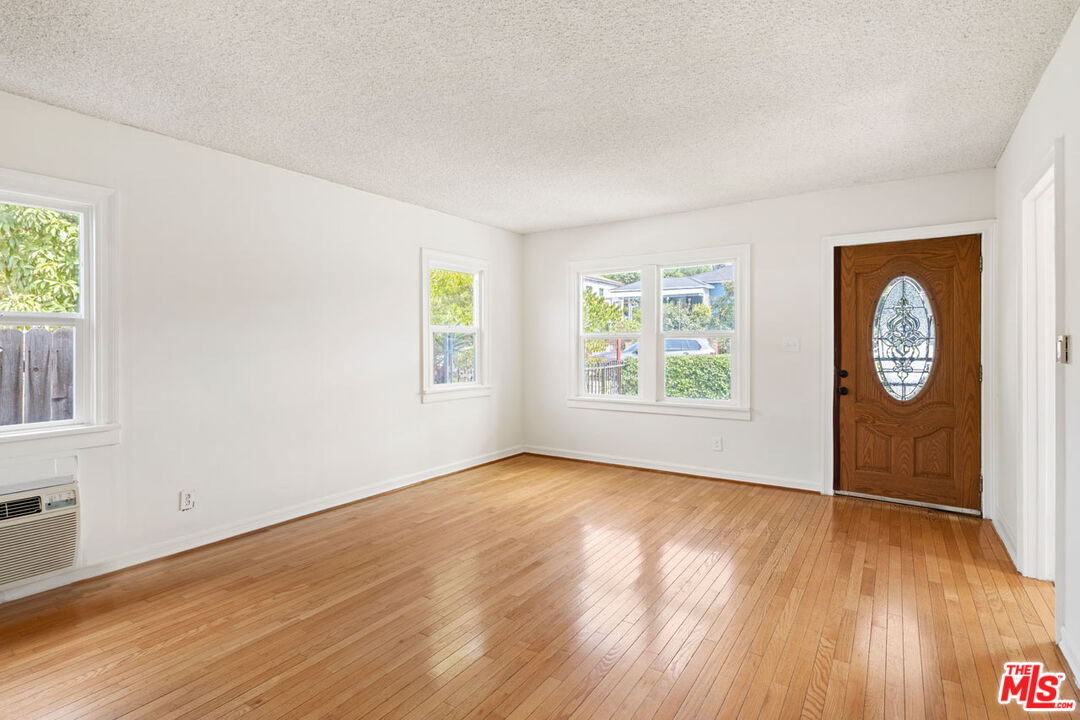 Vacant living room with hardwood floors, multiple windows, and a wooden front door with oval glass.