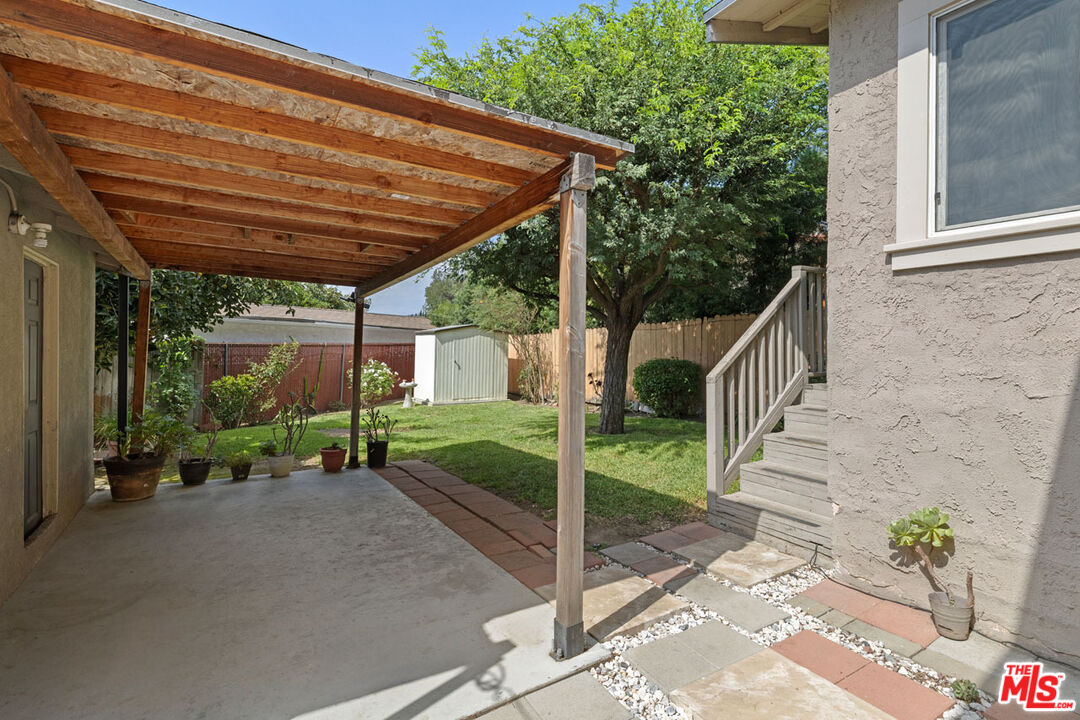 Backyard patio with a timber pergola, paved walkway, lawn, and steps beside the house.