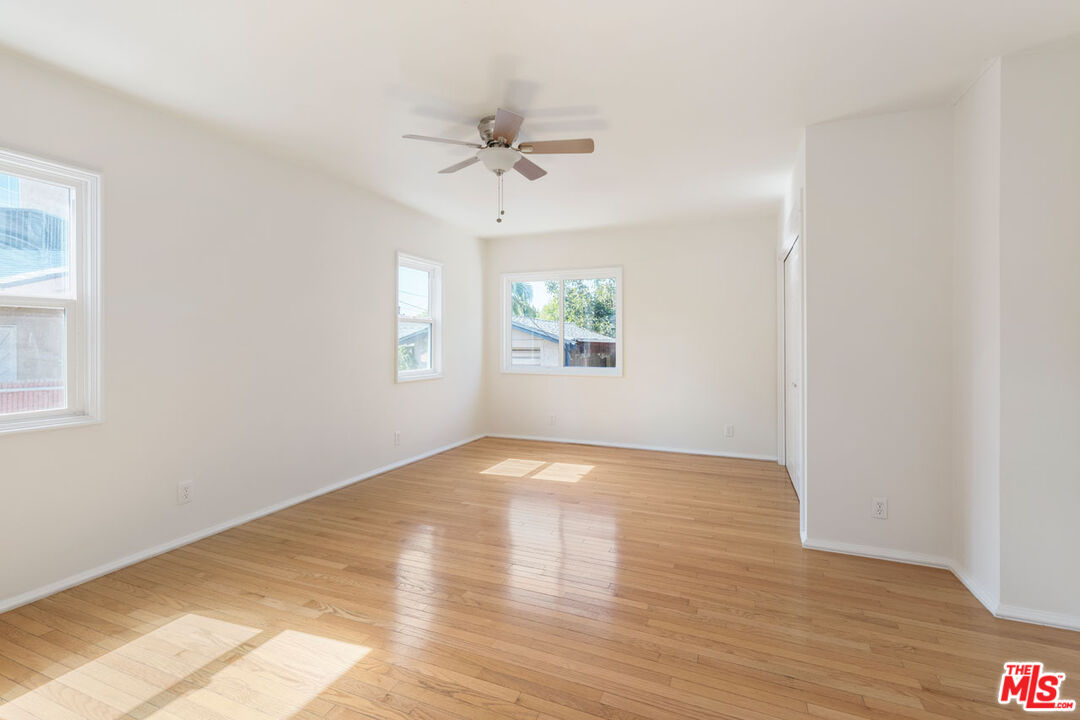 Empty room with hardwood floors, multiple windows, and a ceiling fan.