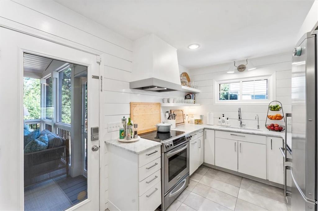 Bright white kitchen with stainless steel appliances and a glass door opening onto a covered porch.