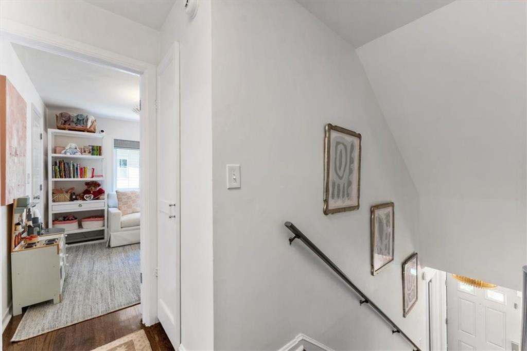 Bright stairwell with a dark handrail and framed artwork, overlooking a furnished room with built-in shelves.