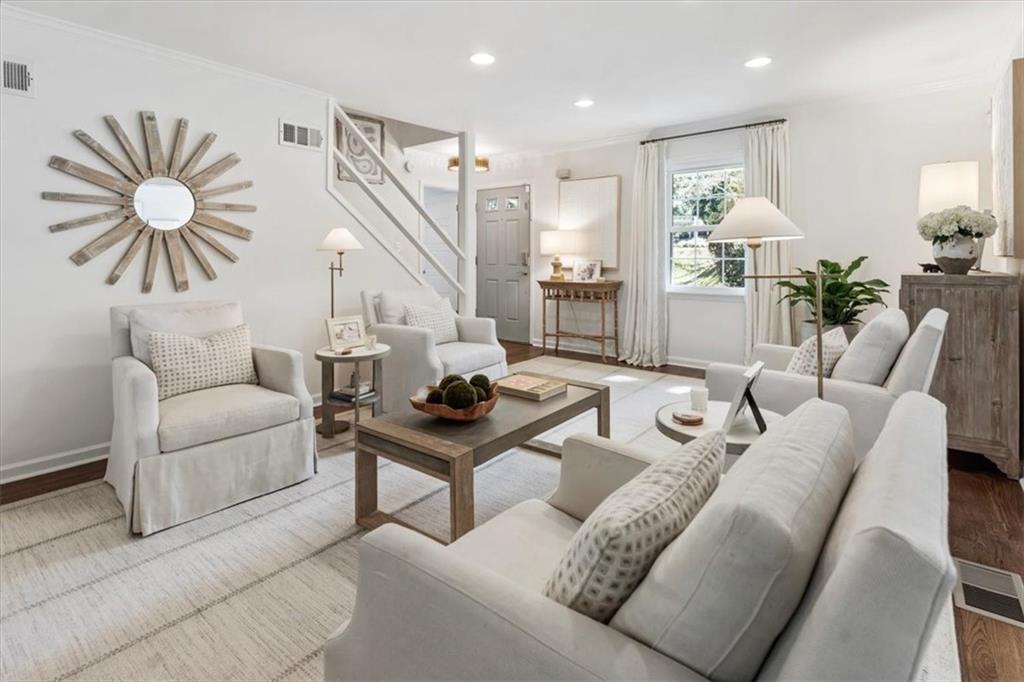 Staged living room with white seating, a staircase, and a large sunburst mirror.