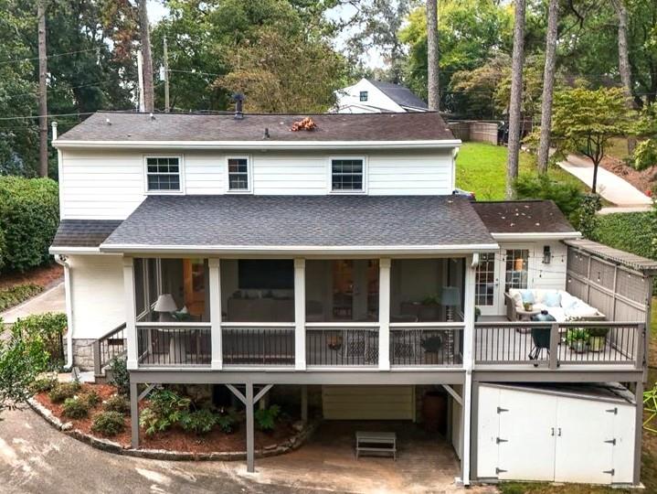 Rear of a white two-story house with a covered raised porch and deck among mature trees.