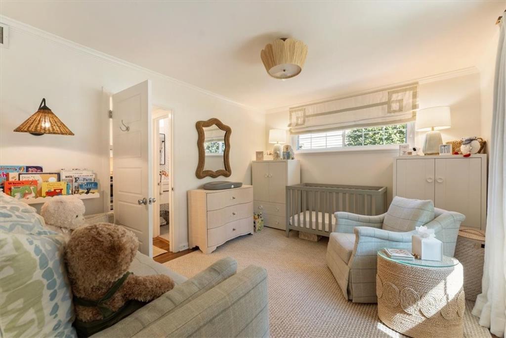 Nursery with a gray crib, white cabinets, and pale upholstered seating beside a wide window.