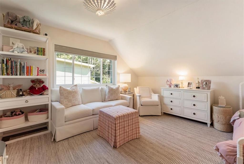Furnished bedroom with a white sofa, built-in bookshelves, and pink checkered ottoman.