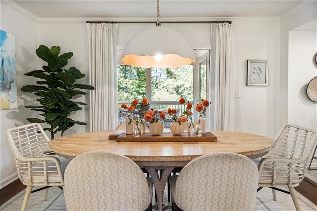 Dining room with an oval wood table, orange-flower centerpiece, and open doors to leafy trees.