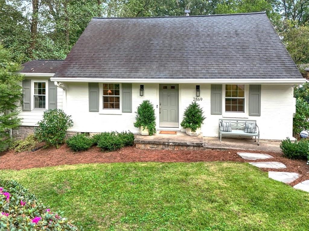 White house with gray shutters, a steep shingle roof, and landscaped front lawn.