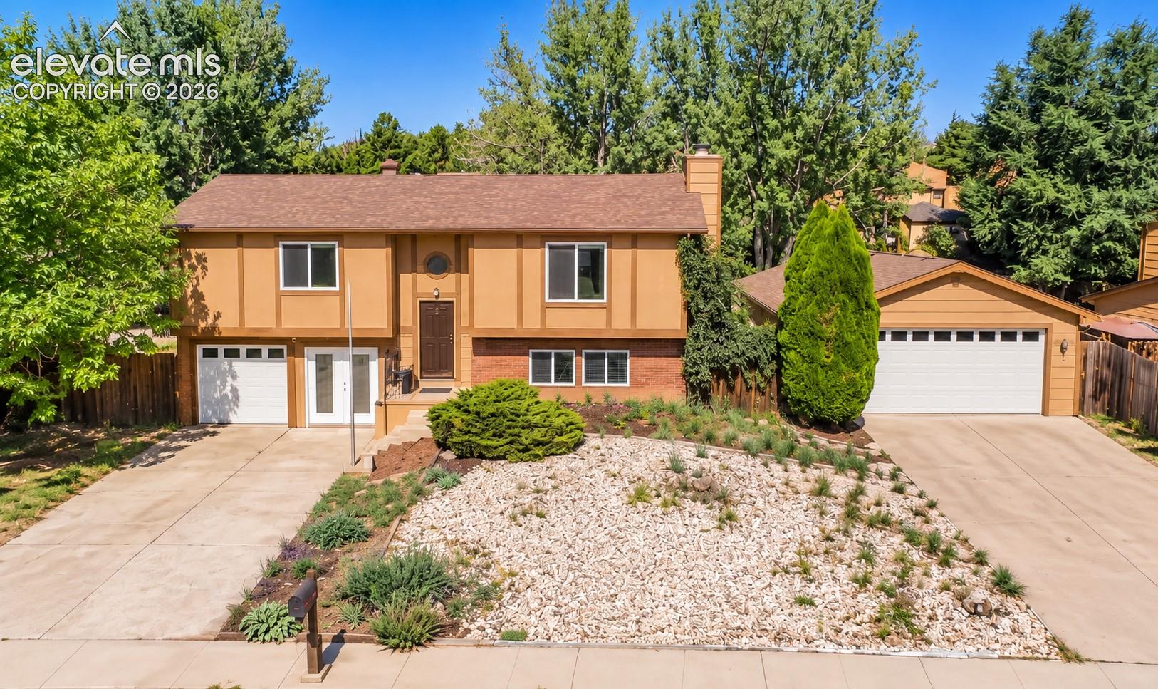Tan split-level home with brick accents, two garage doors, and a rock-landscaped front yard.