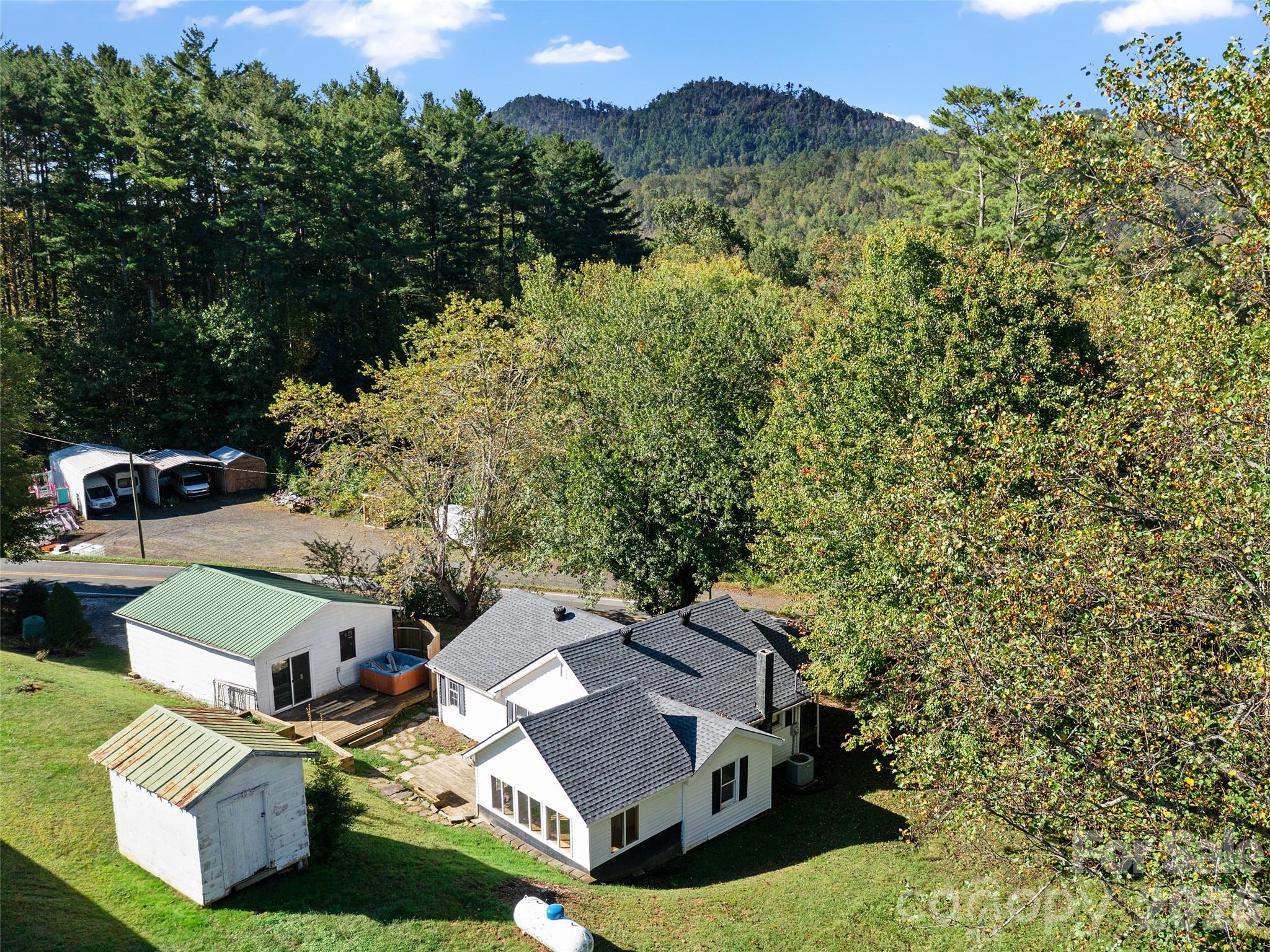 Aerial view of a white house and outbuildings, surrounded by trees with forested mountains beyond.