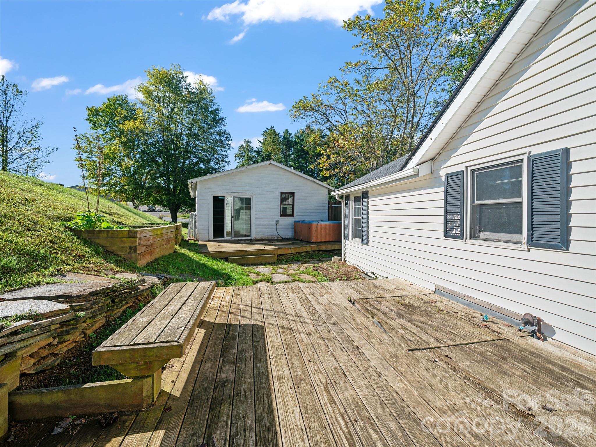 House exterior with a broad wooden deck, raised planter, and detached outbuilding with a hot tub.