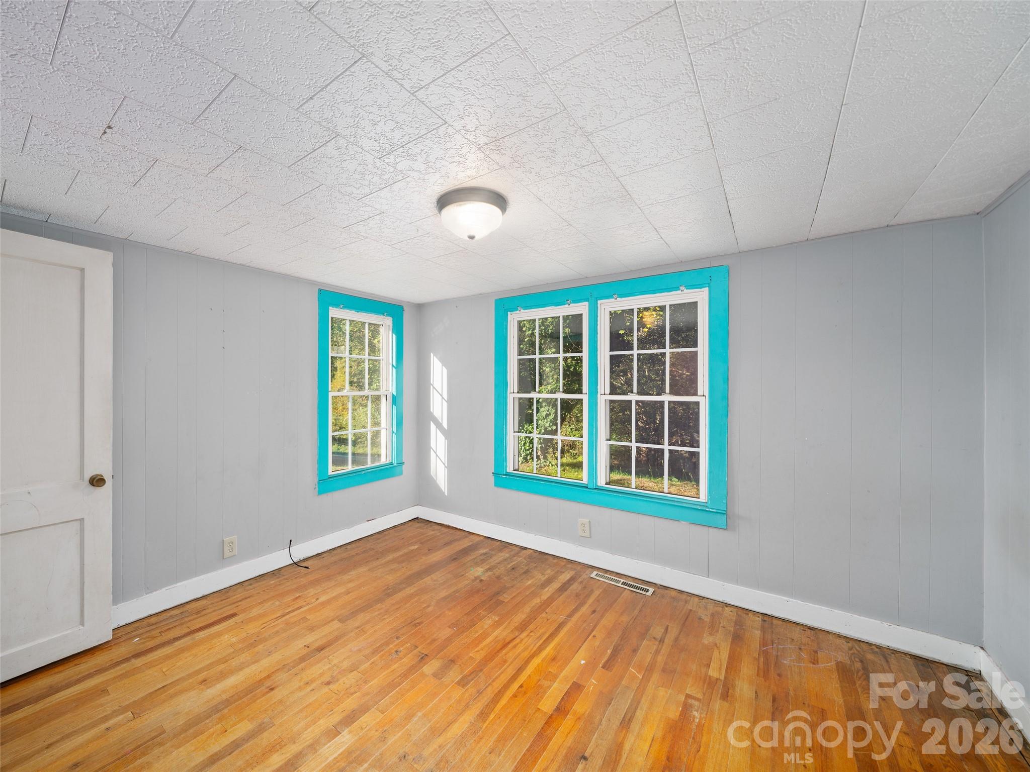 Empty room with hardwood floors and turquoise-trimmed windows.