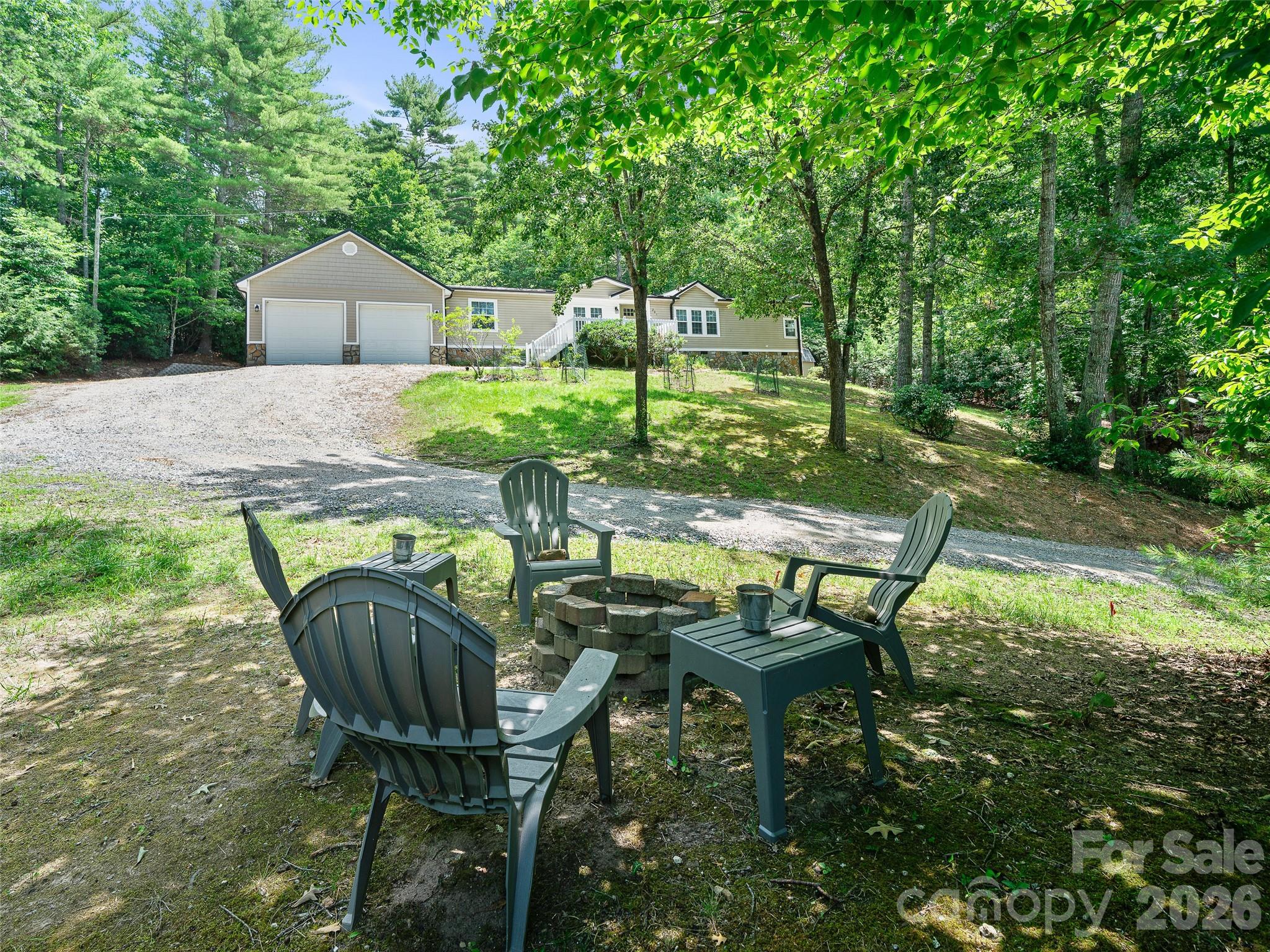 House with attached double garage beyond a wooded yard and outdoor fire-pit seating.