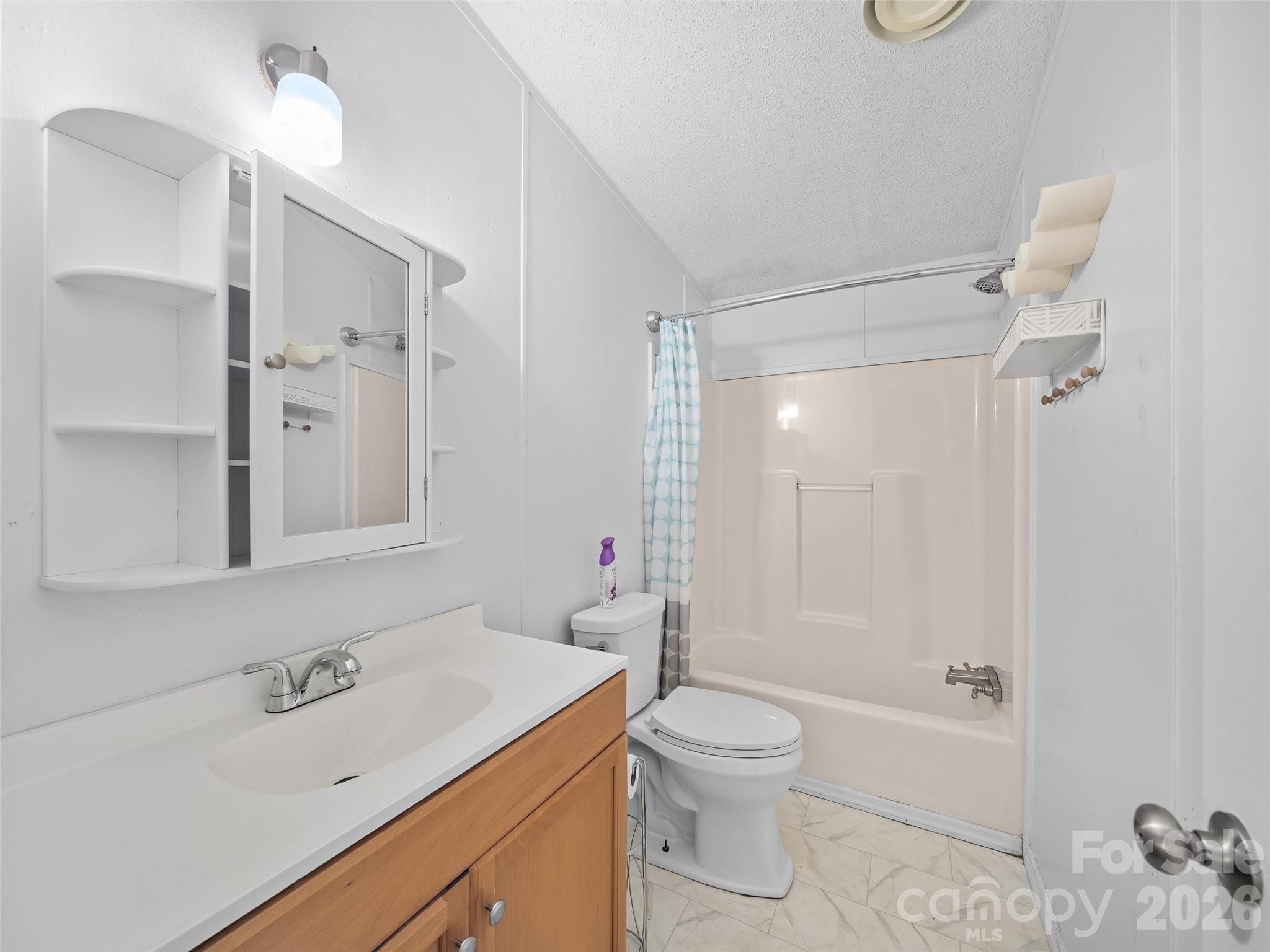 Bathroom with wood vanity, mirrored medicine cabinet, and tub-shower with a blue patterned curtain.