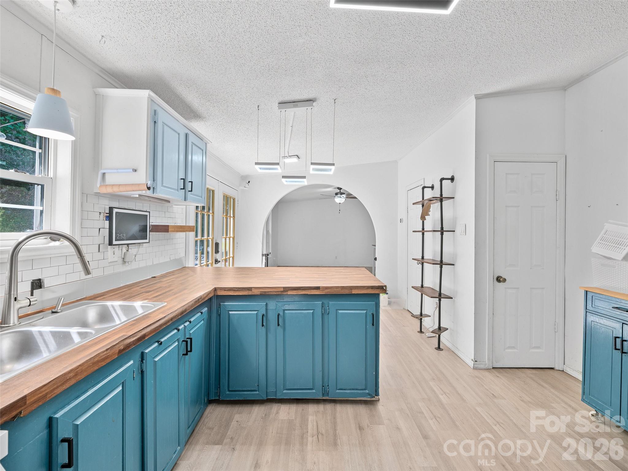 Kitchen with teal-blue cabinets, butcher-block counters, and an arched opening to an adjoining room.