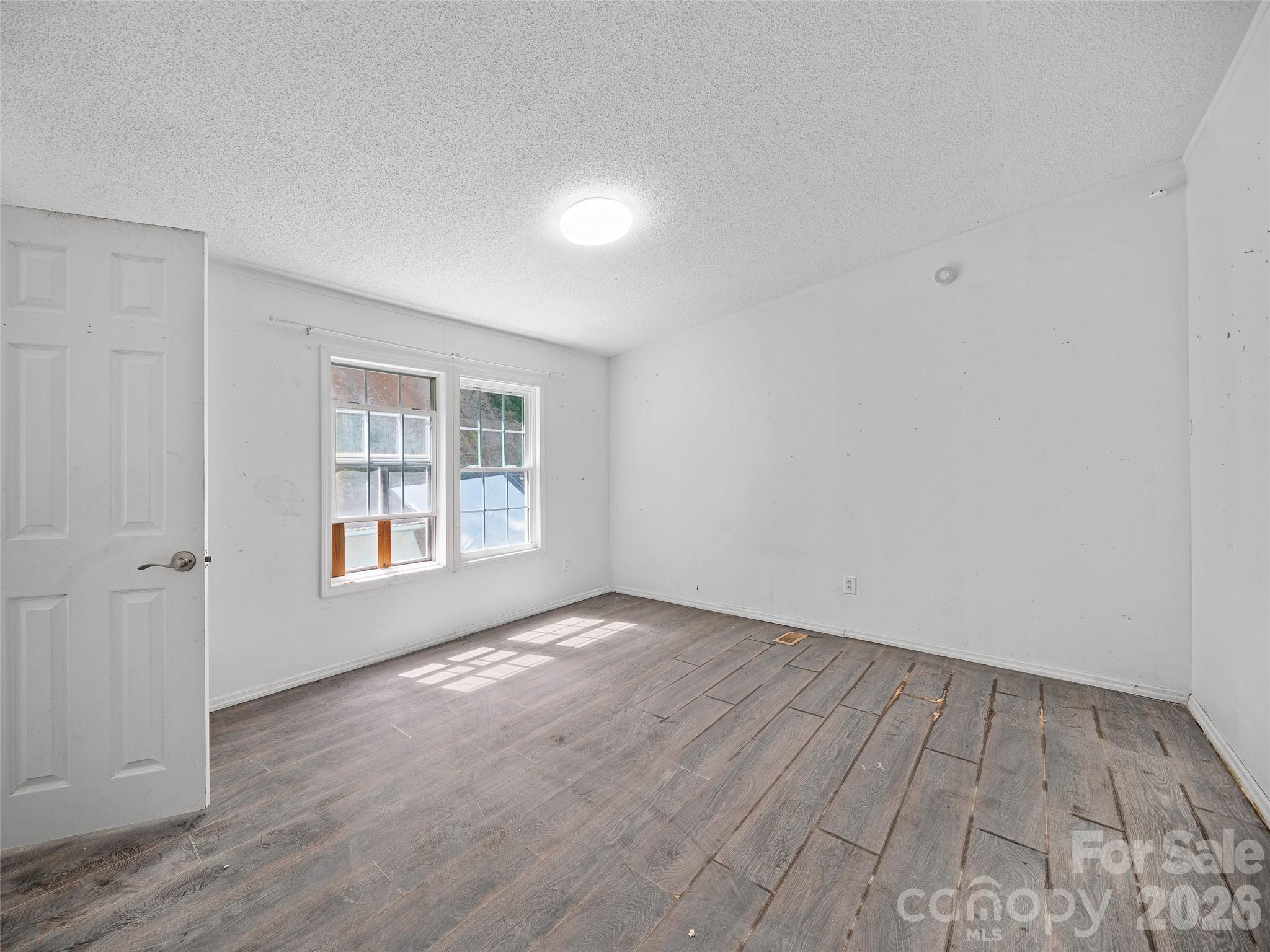 Empty room with two windows and distressed gray-brown plank flooring.