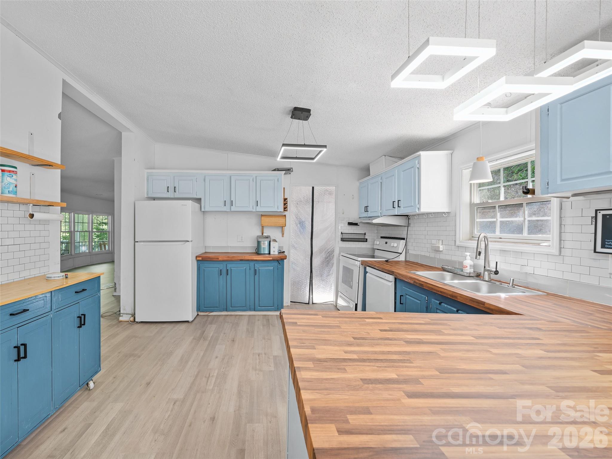 Kitchen with blue cabinets, butcher-block island, wood counters, white appliances and subway tile.