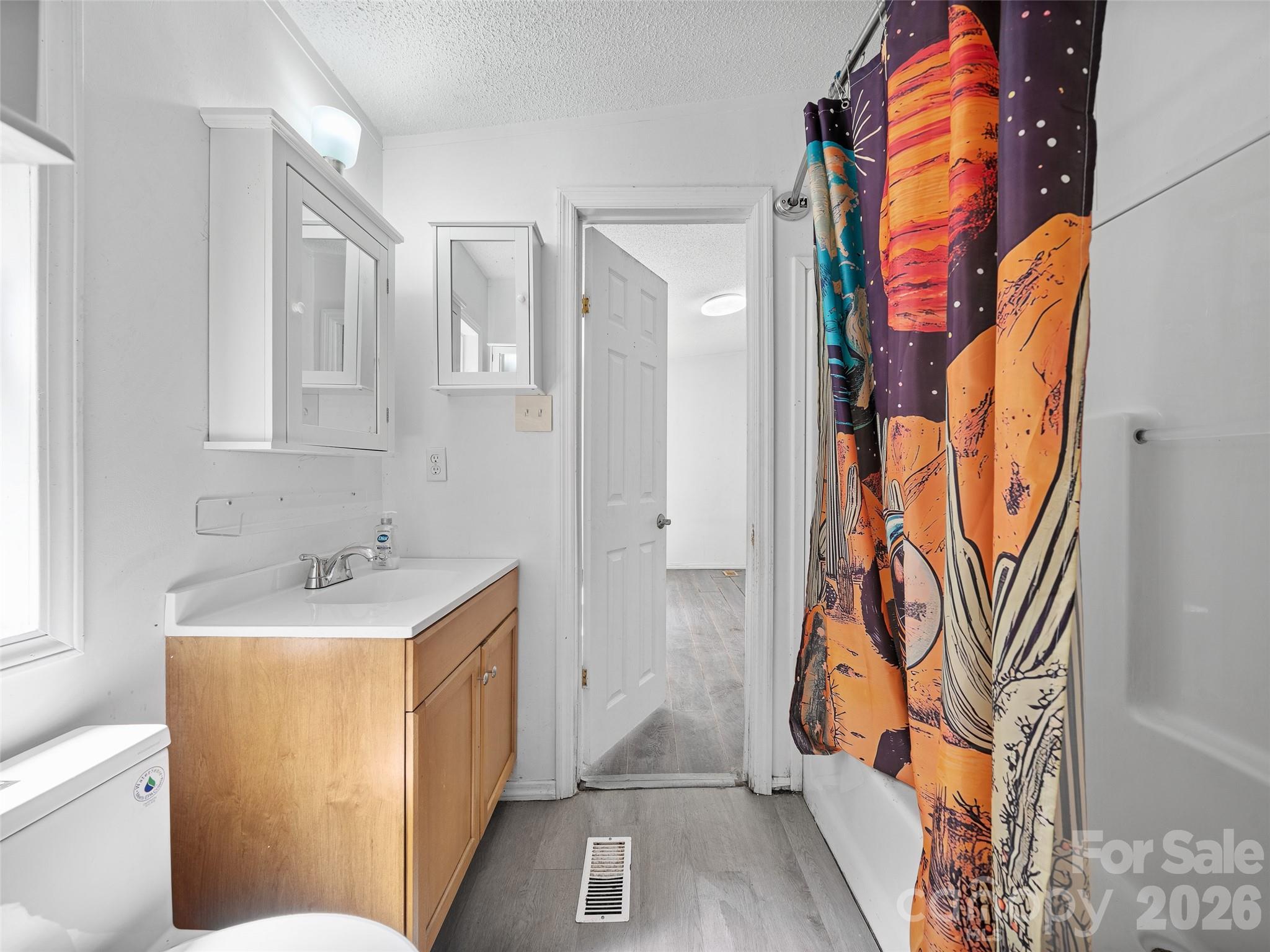 Bathroom with a light wood vanity, mirrored cabinets, and a colorful patterned shower curtain.