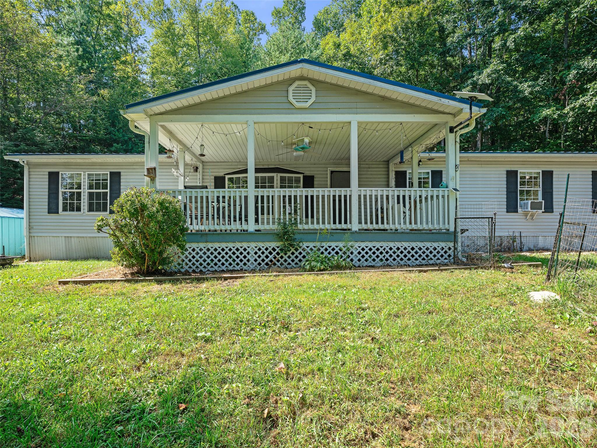 Single-story home with a large covered porch and grassy yard surrounded by trees.