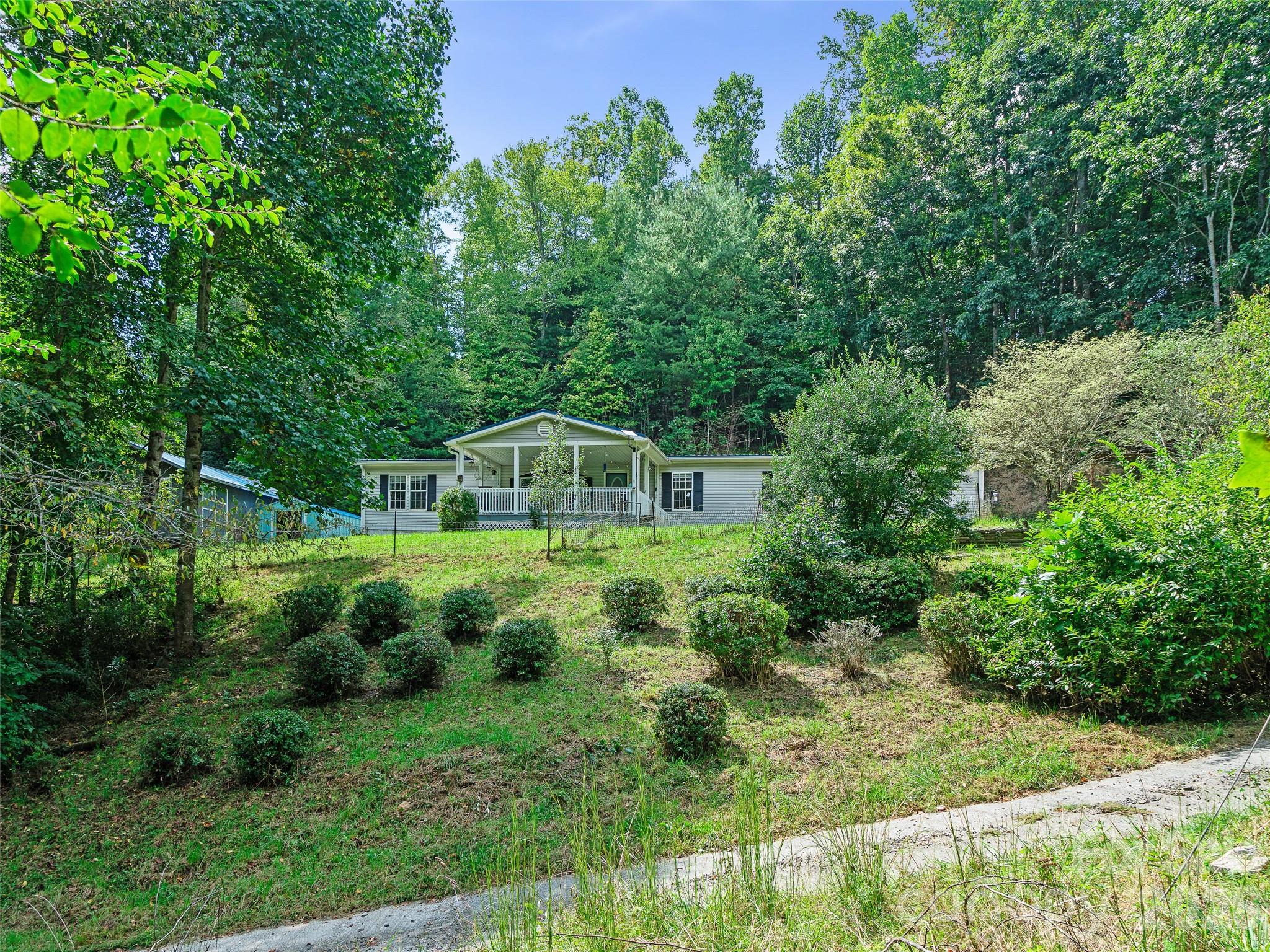 Single-story home with a covered porch on a sloping, wooded lot.