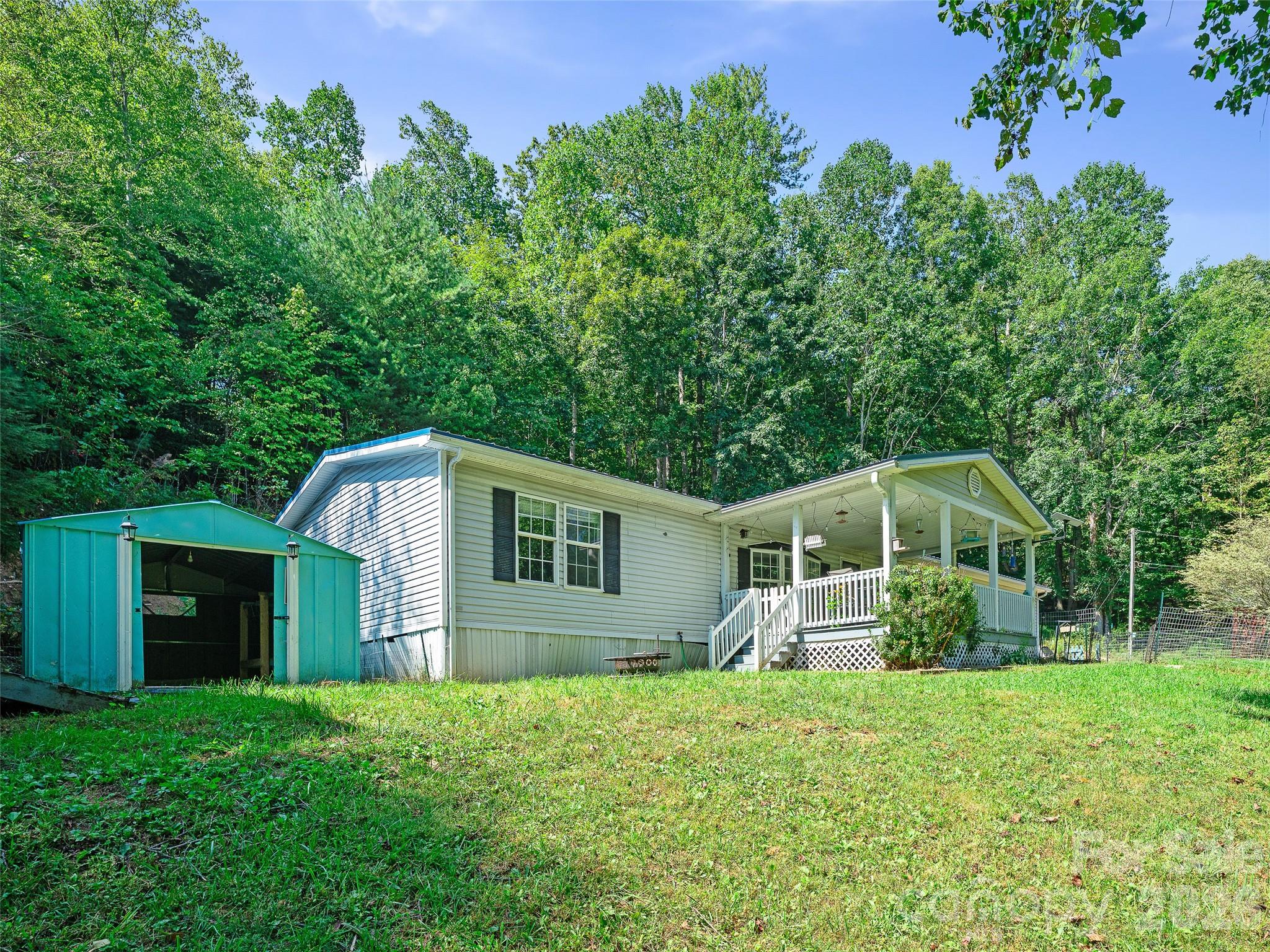 Single-story home with a covered porch and turquoise metal carport on a wooded lot.