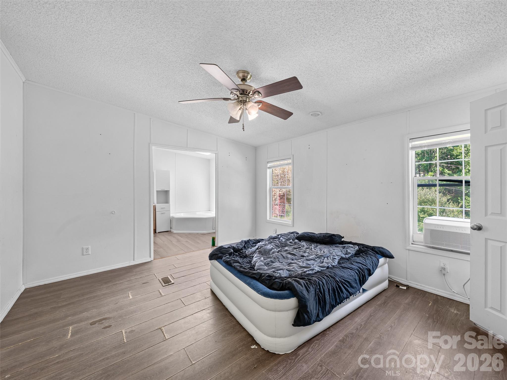 Bedroom with a low air mattress, ceiling fan, wood-look flooring, and an open doorway to a bathroom.