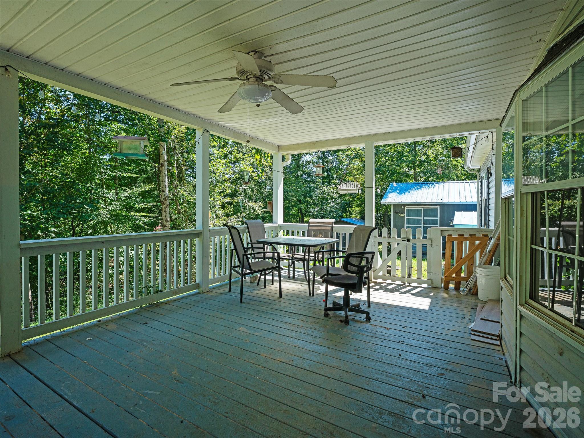 Covered deck with a ceiling fan, outdoor dining set, and wooded views.