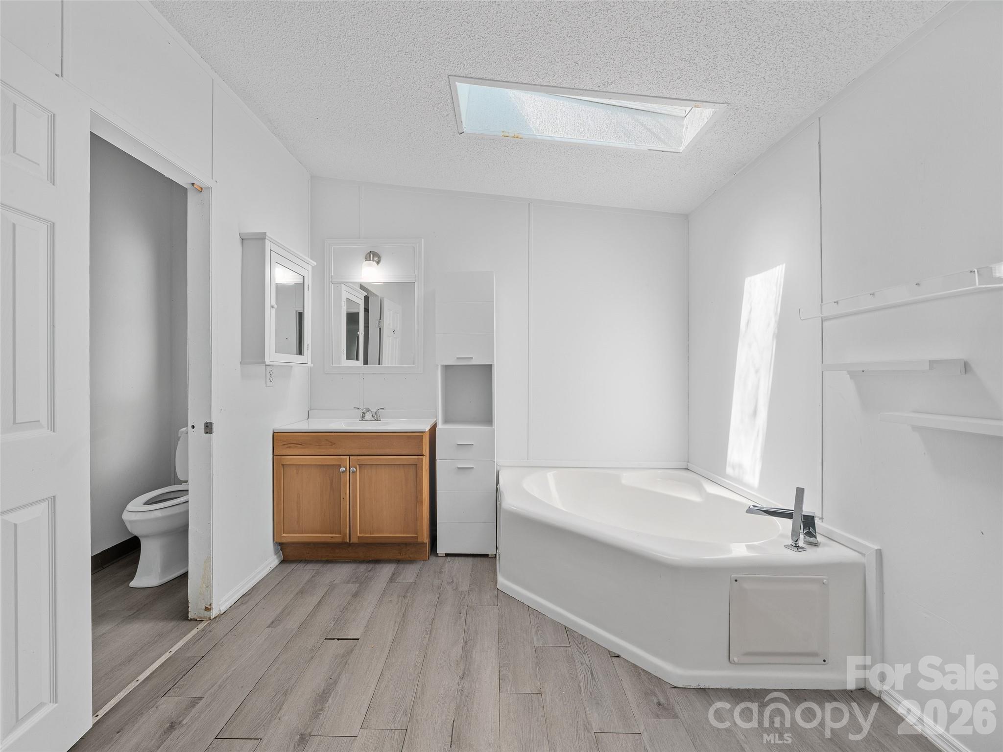 Bathroom with a corner soaking tub, wood vanity, and toilet nook.