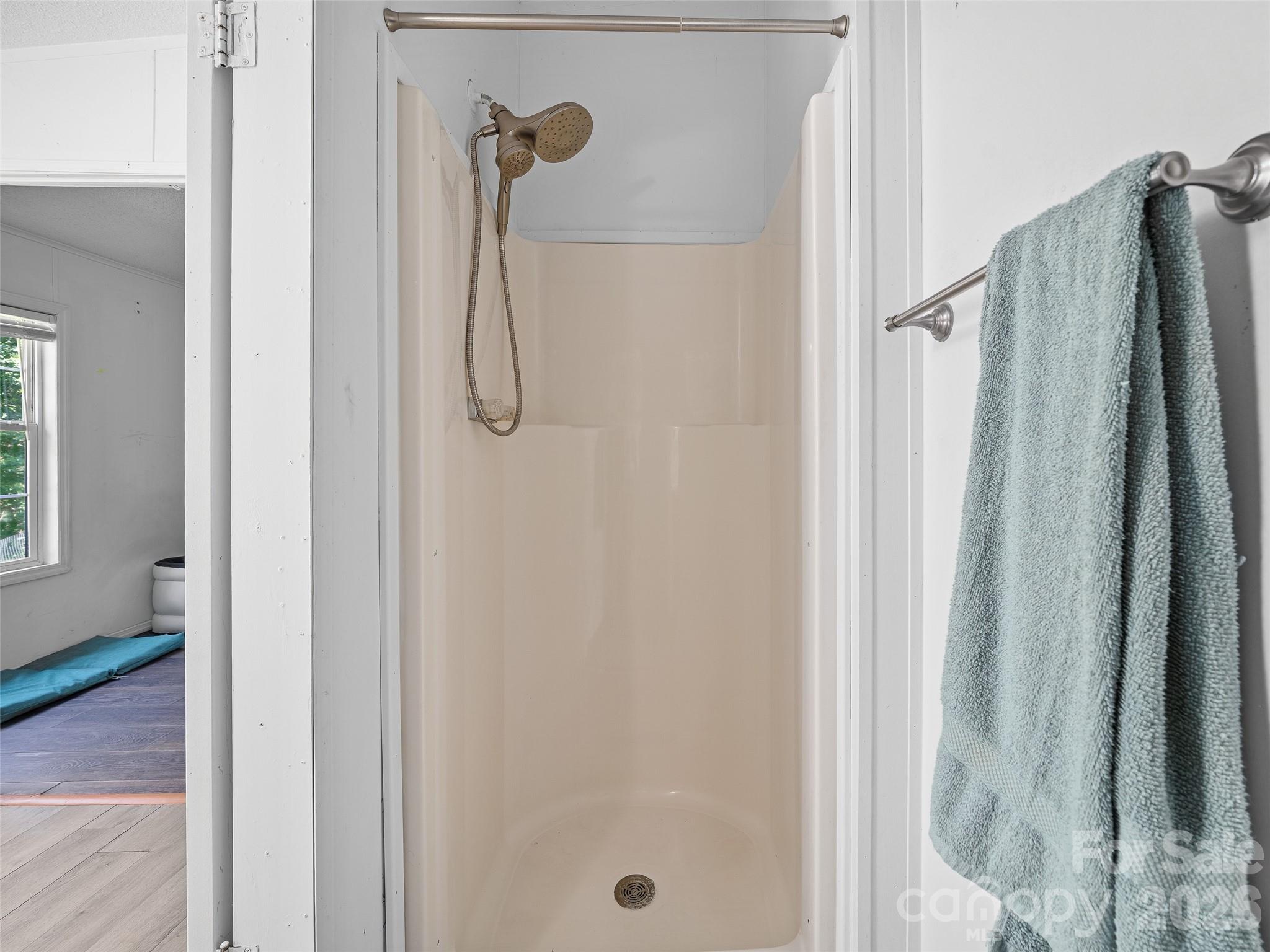 White shower stall with handheld showerhead and a blue towel hanging beside it.