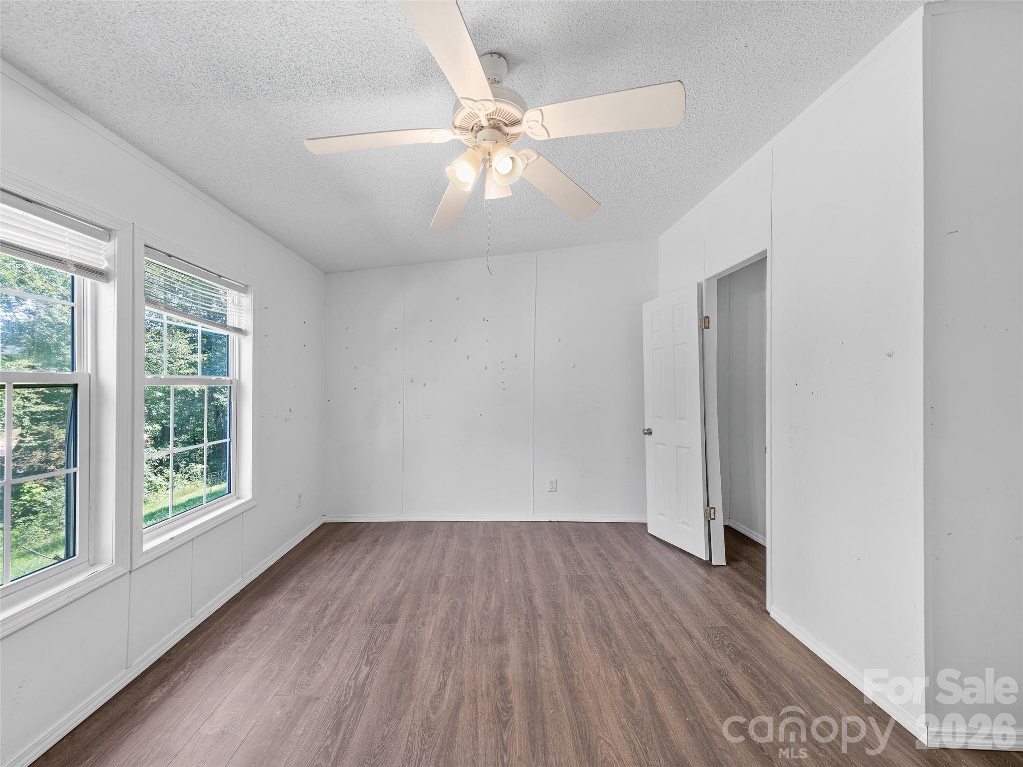Empty room with wood-look flooring, two windows, and a ceiling fan.
