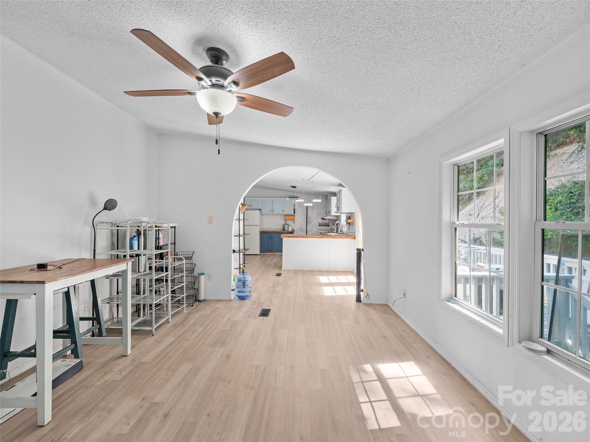 Dining area with an arched opening to a blue-and-white kitchen and large sunlit windows.