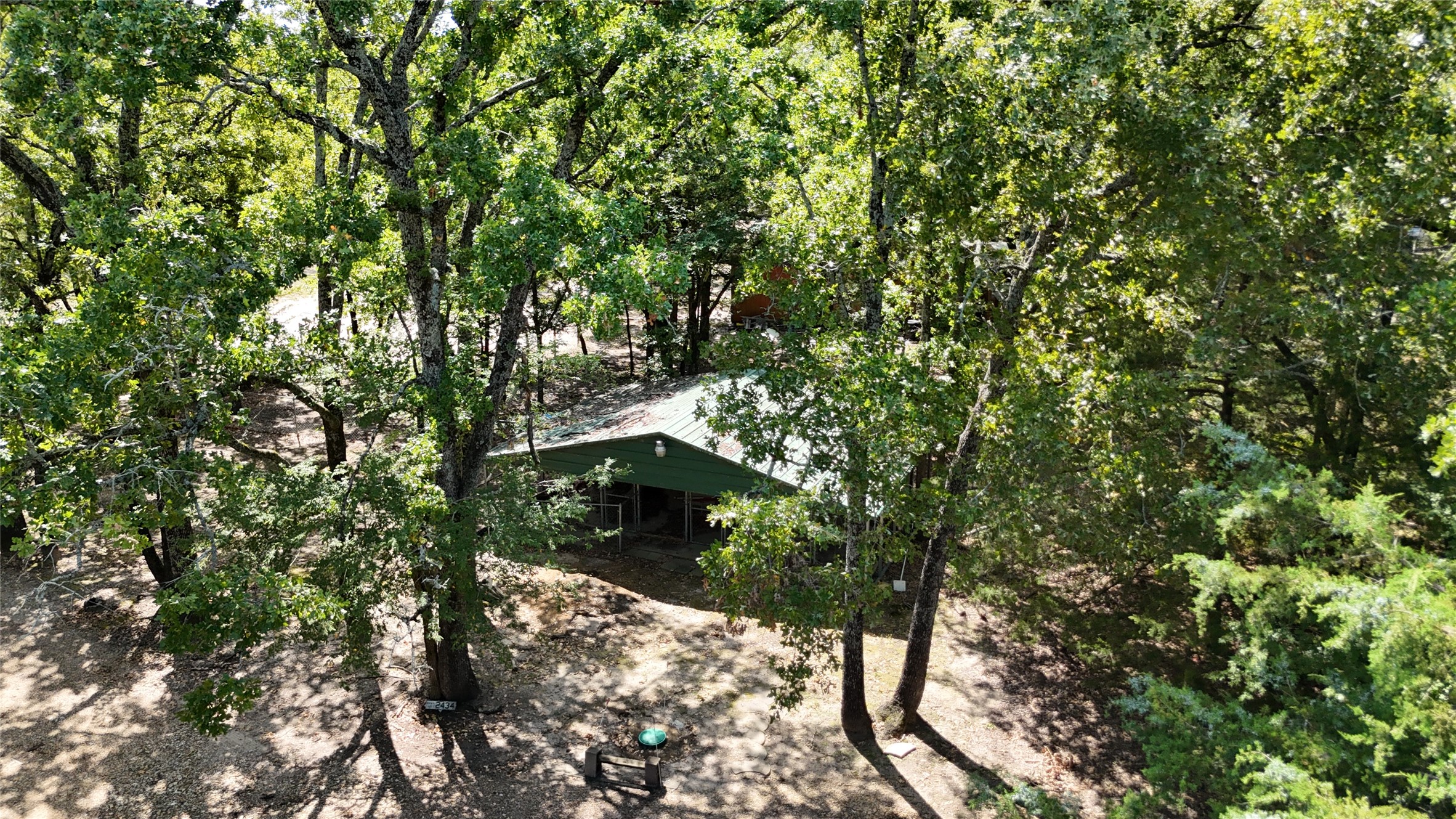 Aerial view of a green-roofed home surrounded by dense trees on a wooded lot.