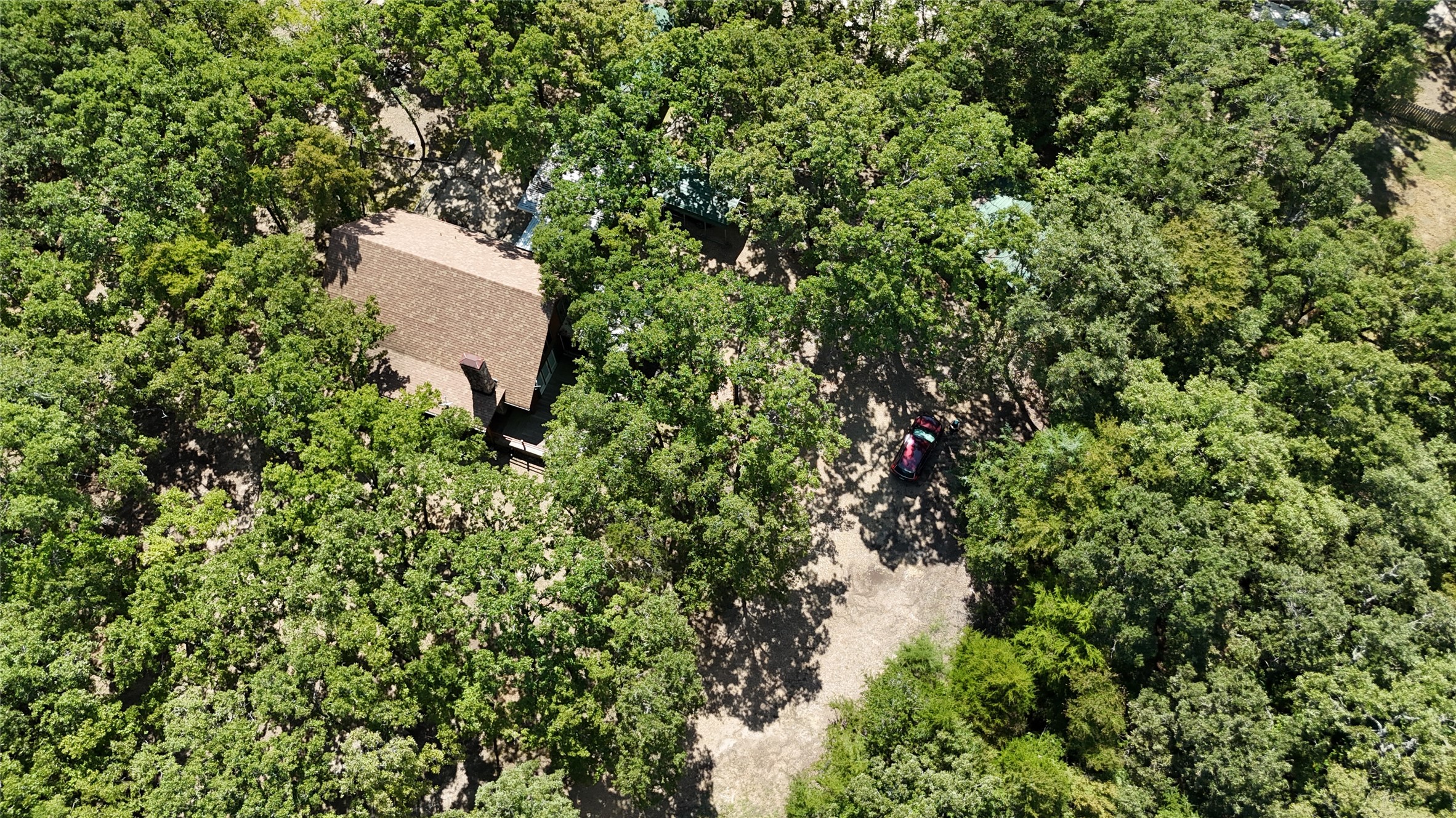 Aerial view of a tree-covered property with a home and gravel driveway.