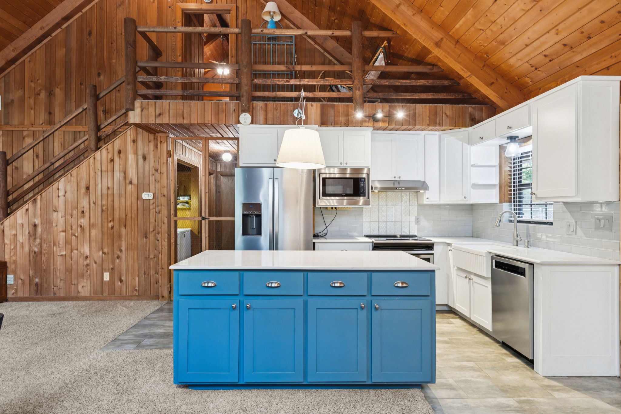 Kitchen with a vivid blue island, white cabinets, stainless appliances, and exposed timber beams above.