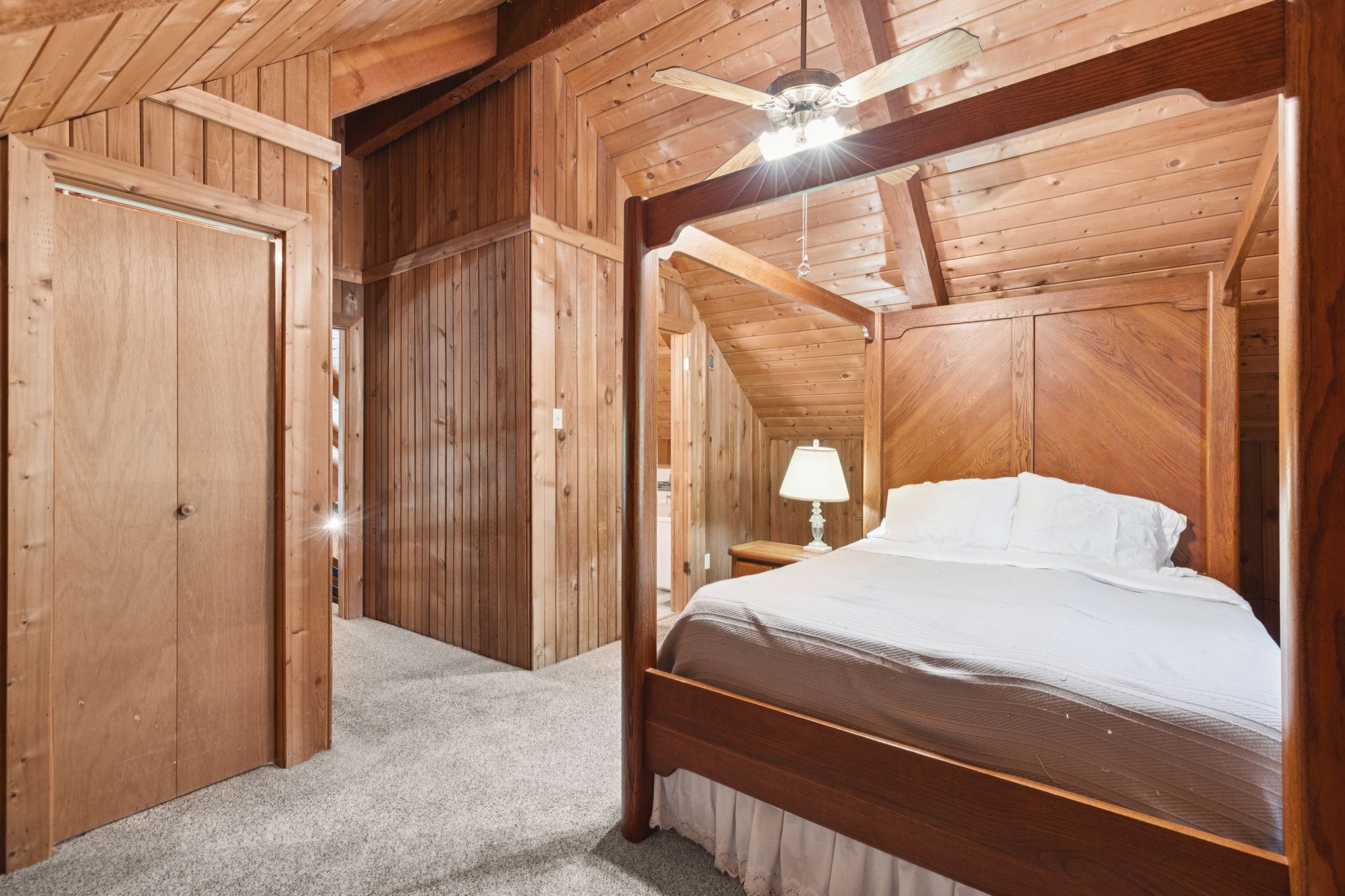 Wood-paneled bedroom with a vaulted beam ceiling, ceiling fan, and dark wooden bed with white bedding.
