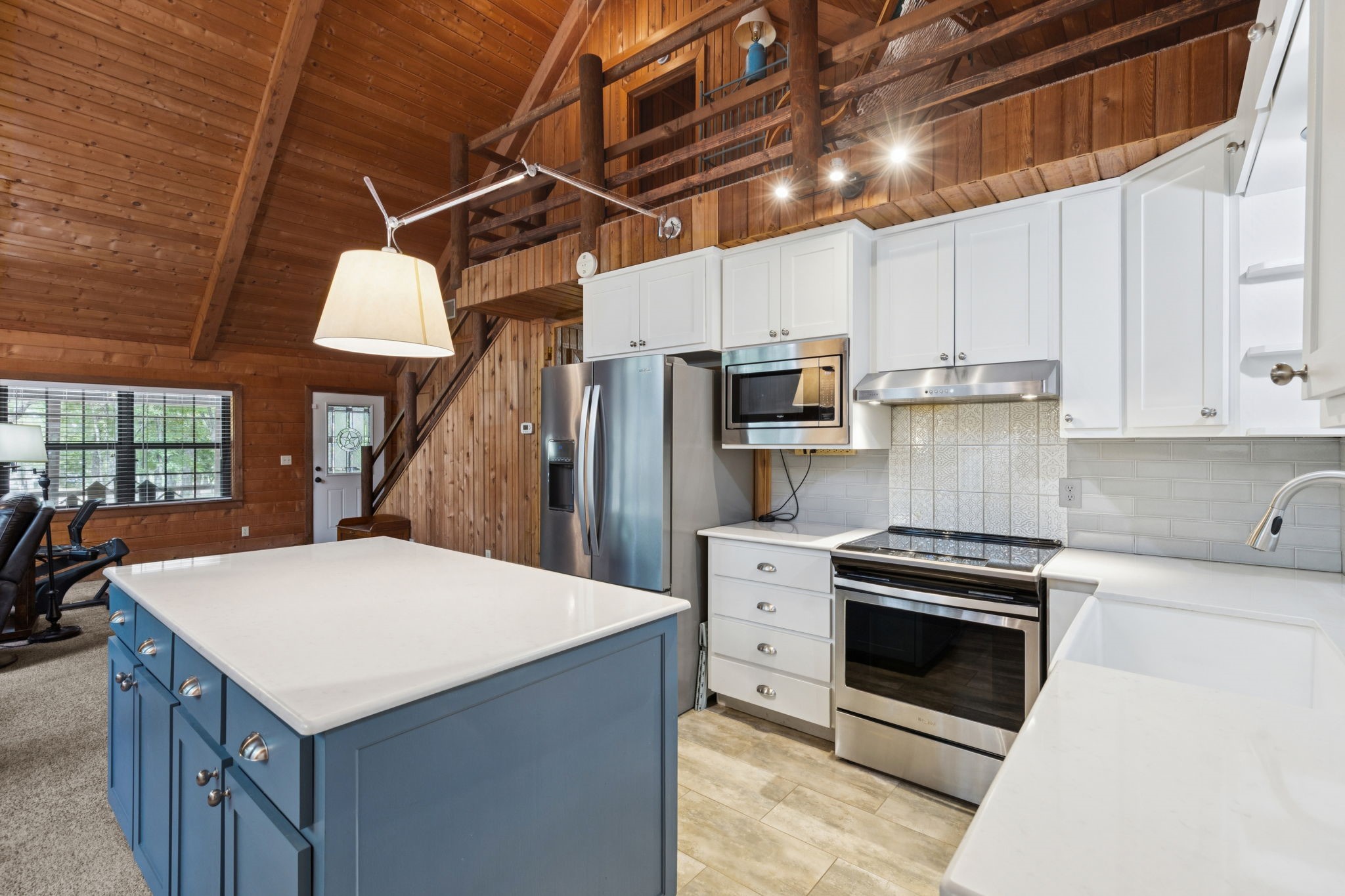 Kitchen with blue island, stainless steel appliances, and a wood-paneled vaulted ceiling and loft.