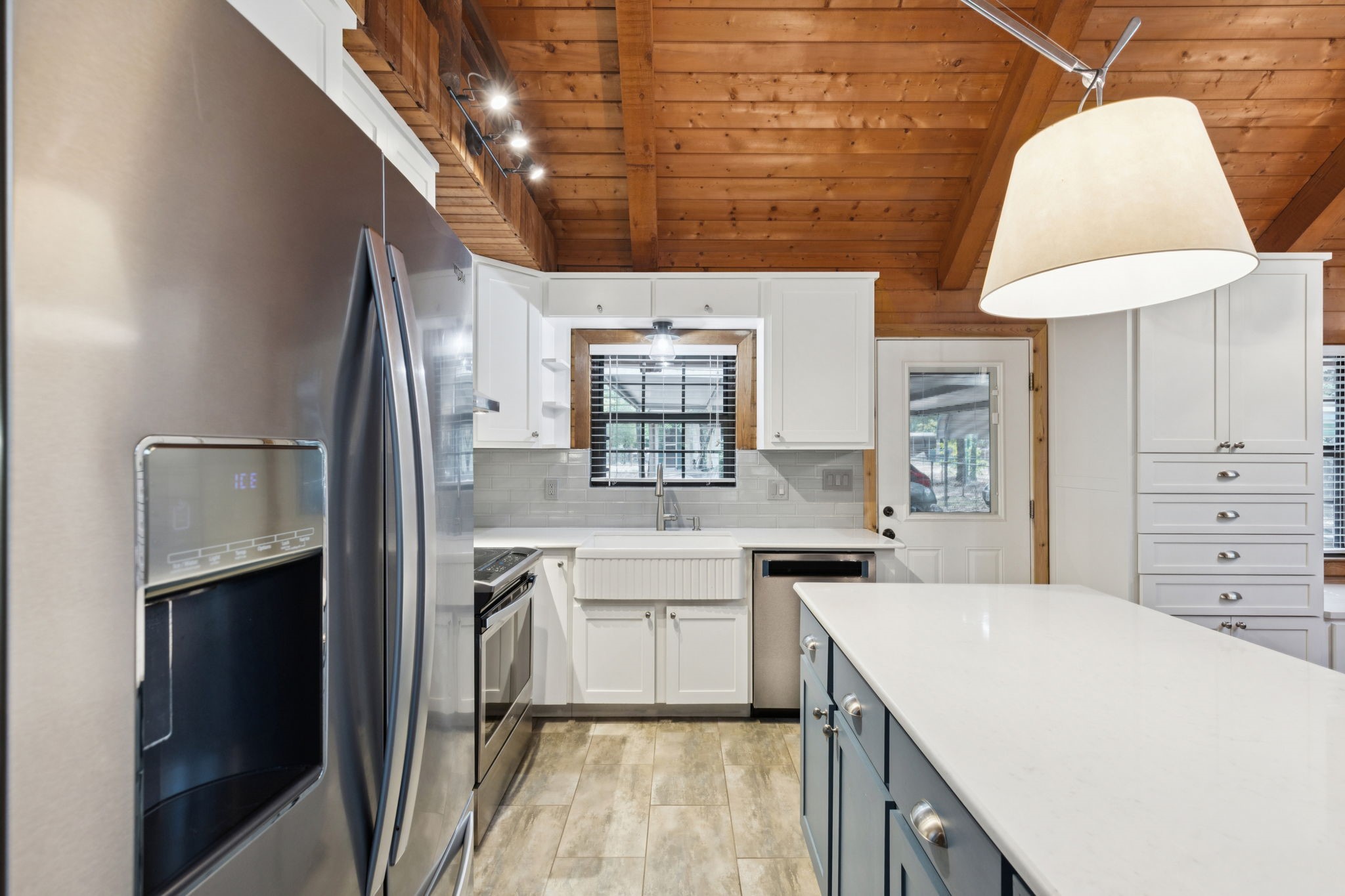 Kitchen with a white island, farmhouse sink, stainless steel appliances, and exposed wood ceiling.