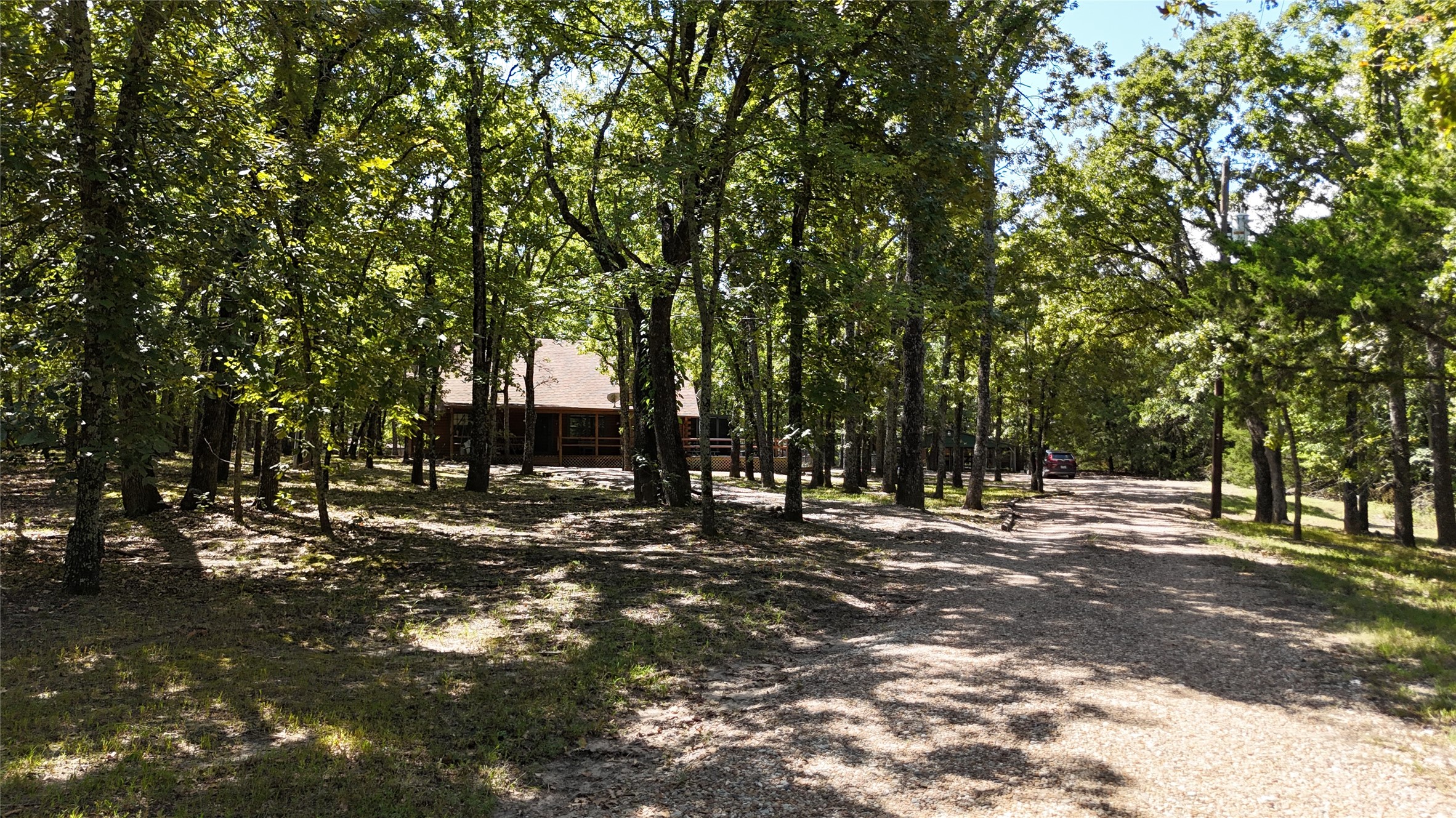 Wooded home with a covered porch beside a broad gravel driveway.