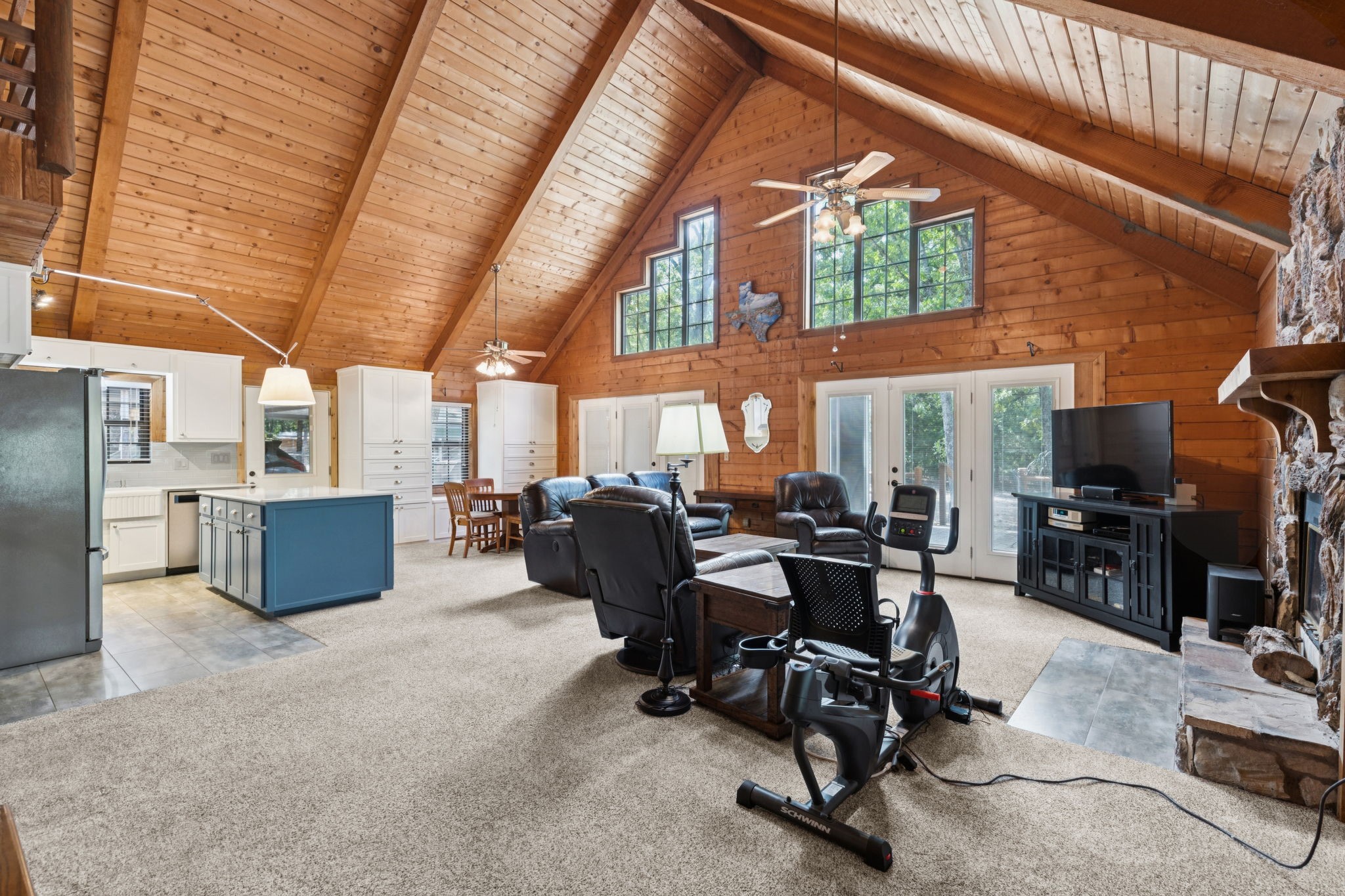 Open living room and kitchen with a vaulted wood ceiling, blue island, leather seating, and stone fireplace.