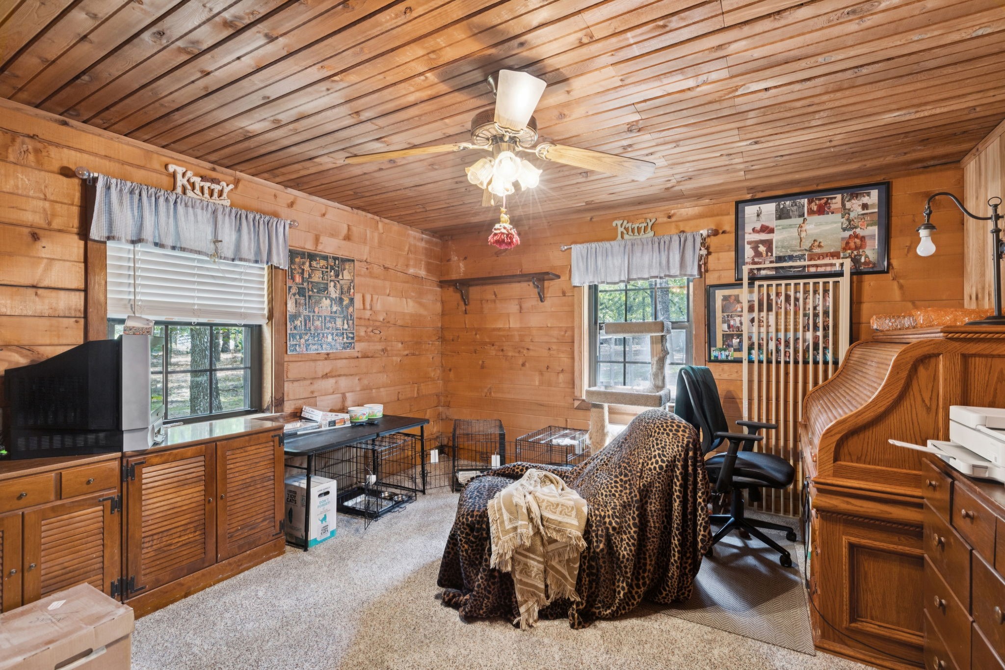 Wood-paneled room with a desk, piano, cat tree, and pet crates.