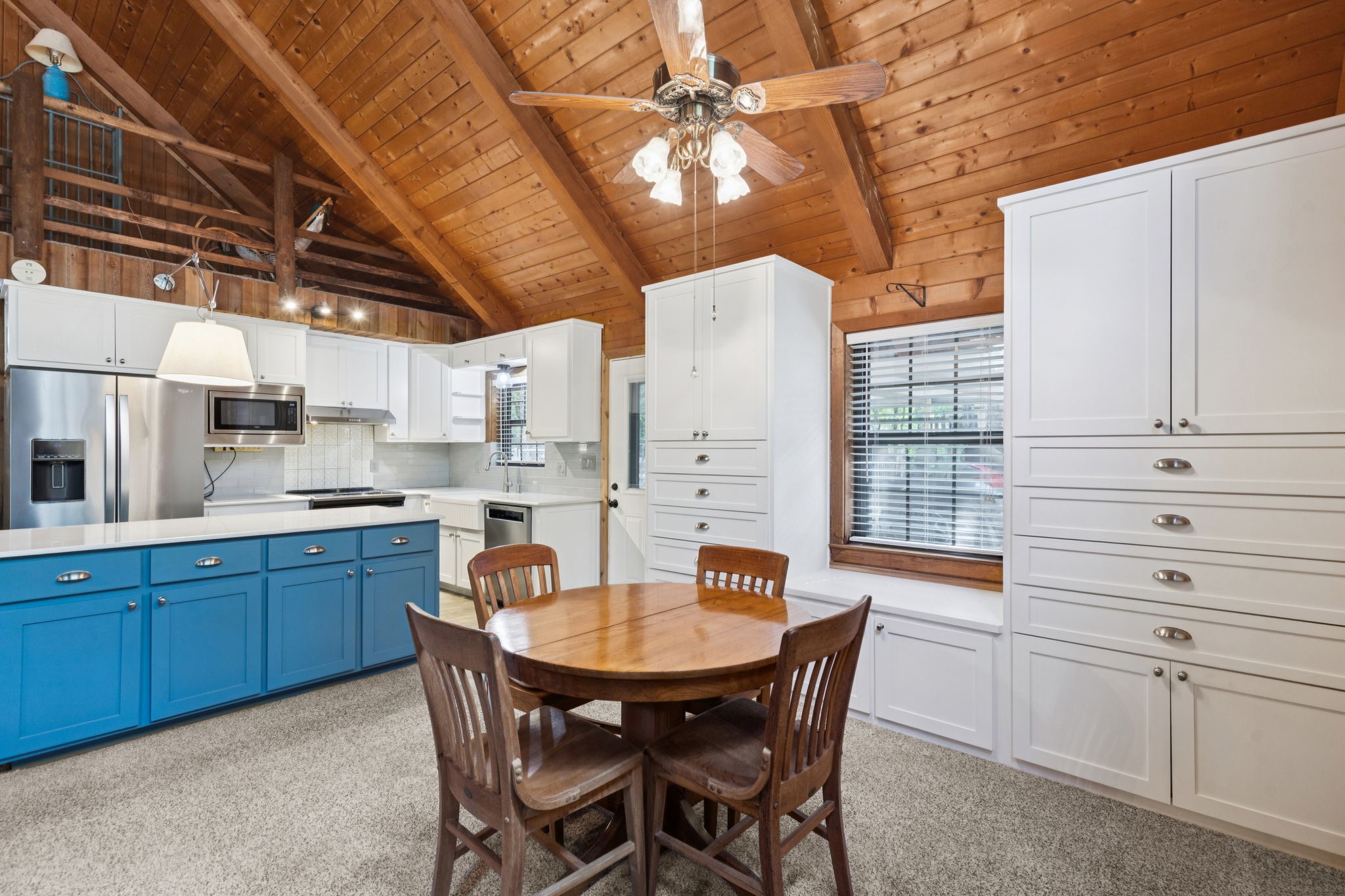 Kitchen with blue island, white cabinets, round wooden table, and vaulted wood ceiling.